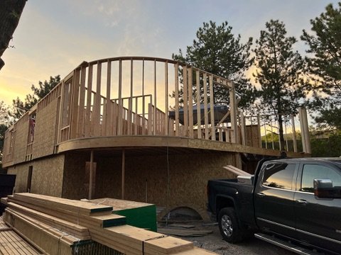 Curved second-story framing at sunset with lumber staged on site